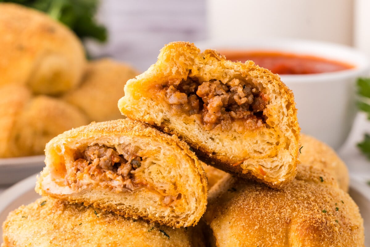 Stuffed bread rolls filled with ground meat, stacked with marinara sauce in the background.