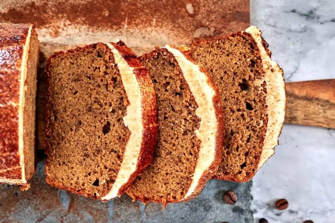 Three slices of glazed loaf cake are arranged on a cutting board next to the rest of the unsliced loaf.