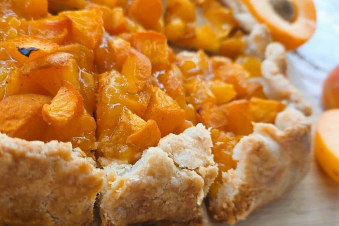 Close-up of a rustic apricot tart with golden crust and juicy, diced apricots on top.