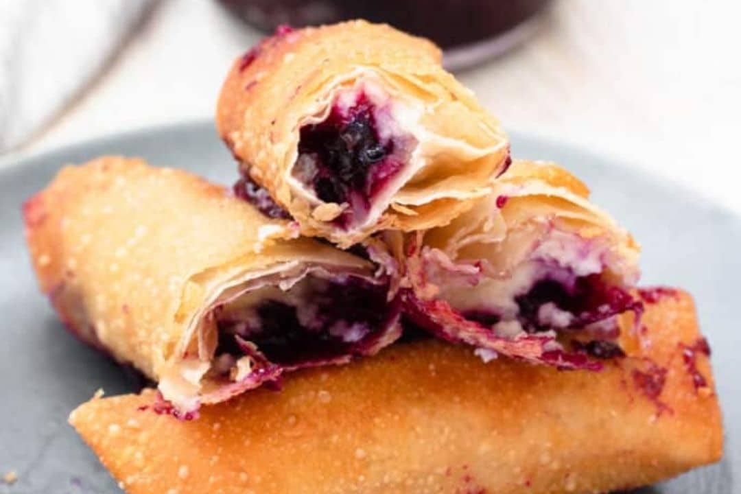 Three golden-brown pastry rolls filled with purple berry filling, stacked on a blue plate.