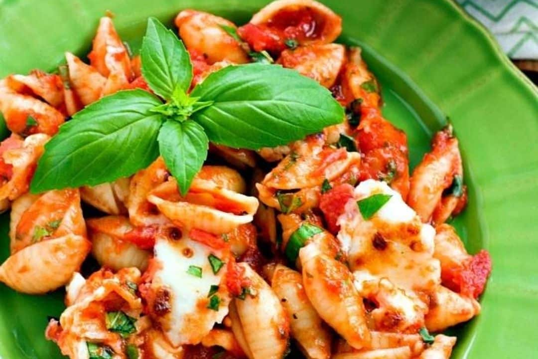 Shell pasta with tomato sauce, mozzarella, herbs, and a basil garnish on a green plate.