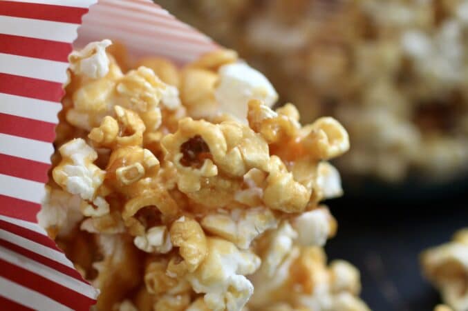 Caramel popcorn spilling from a red and white striped bag.