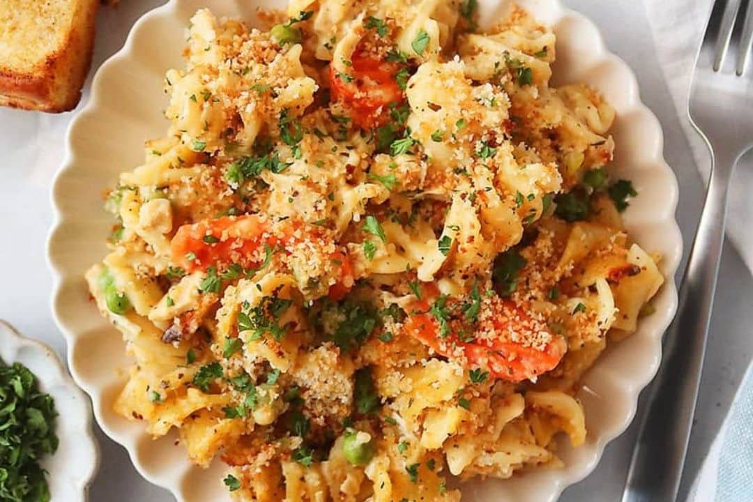 A plate of creamy pasta with peas, carrots, breadcrumbs, and fresh parsley, served with a fork.