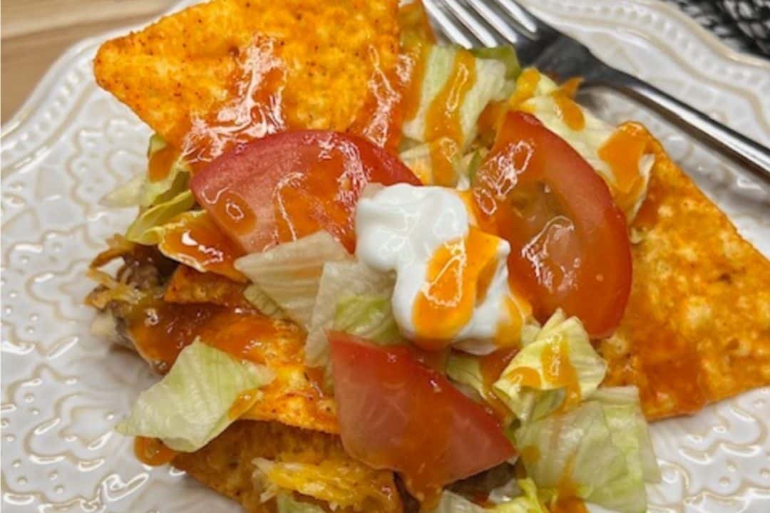 Plate of taco salad with chips, lettuce, tomato, shredded cheese, sour cream, and orange sauce.