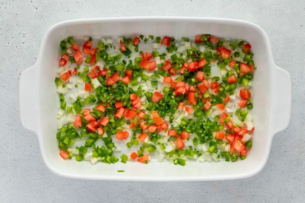 A white baking dish containing diced tomatoes, onions, and green peppers.