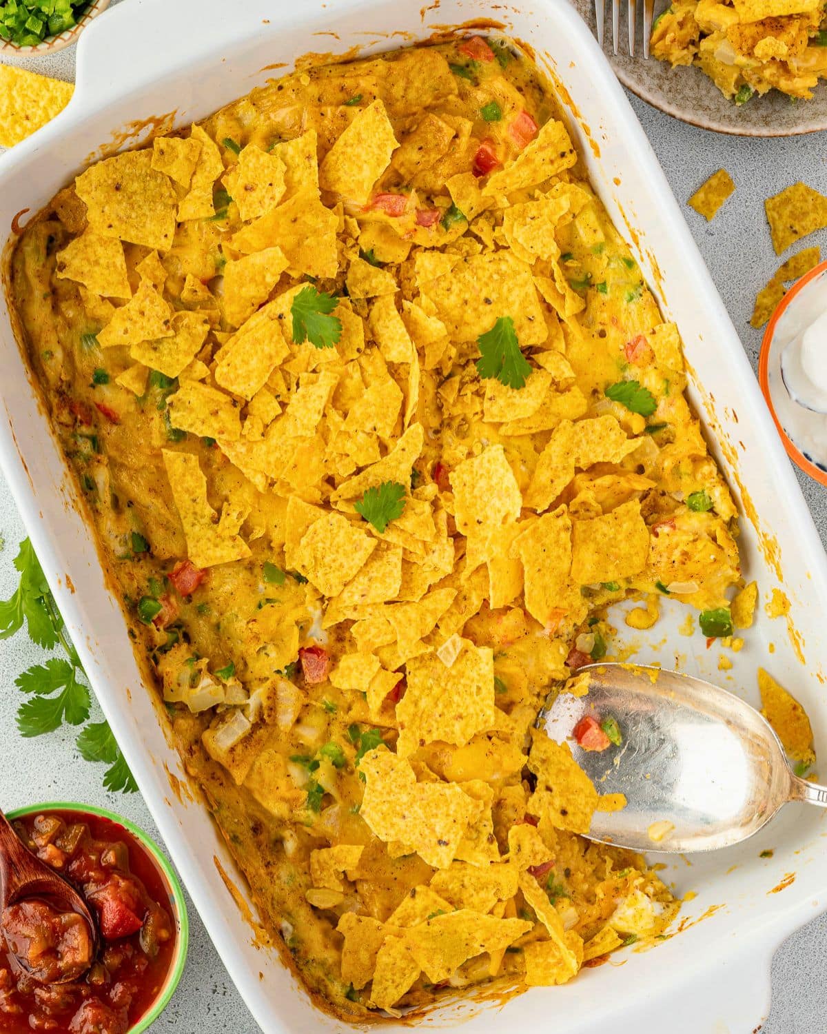 A rectangular baking dish filled with cheesy vegetable casserole topped with crushed tortilla chips.