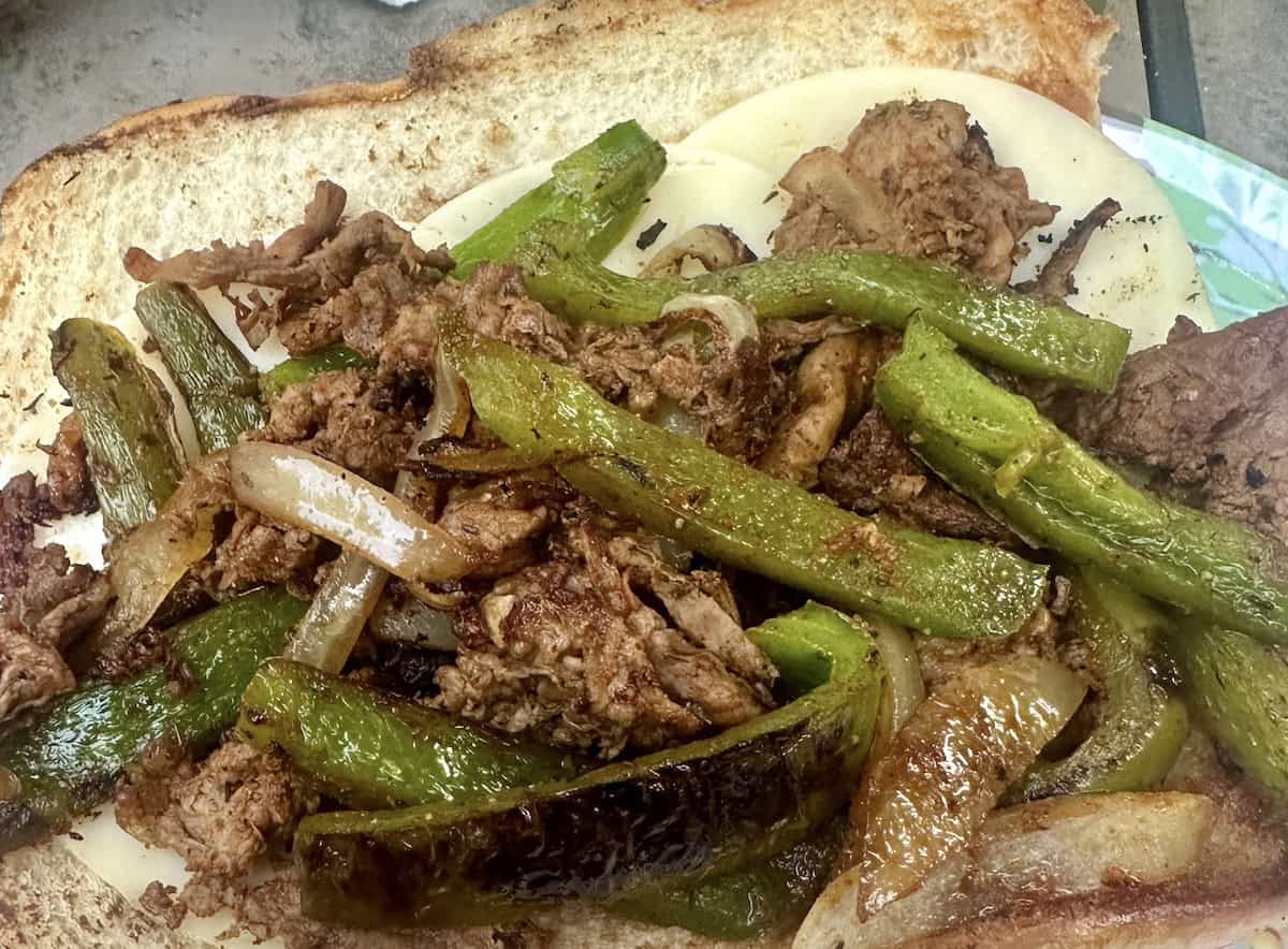 Sliced steak, grilled green peppers, onions, and melted cheese on a hoagie roll.