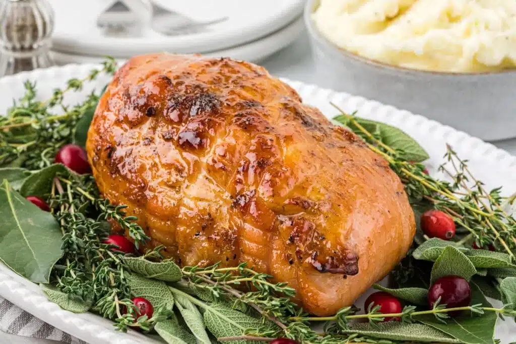 A golden roasted vegan holiday loaf on herbs, with cranberries and a bowl of mashed potatoes in the background.
