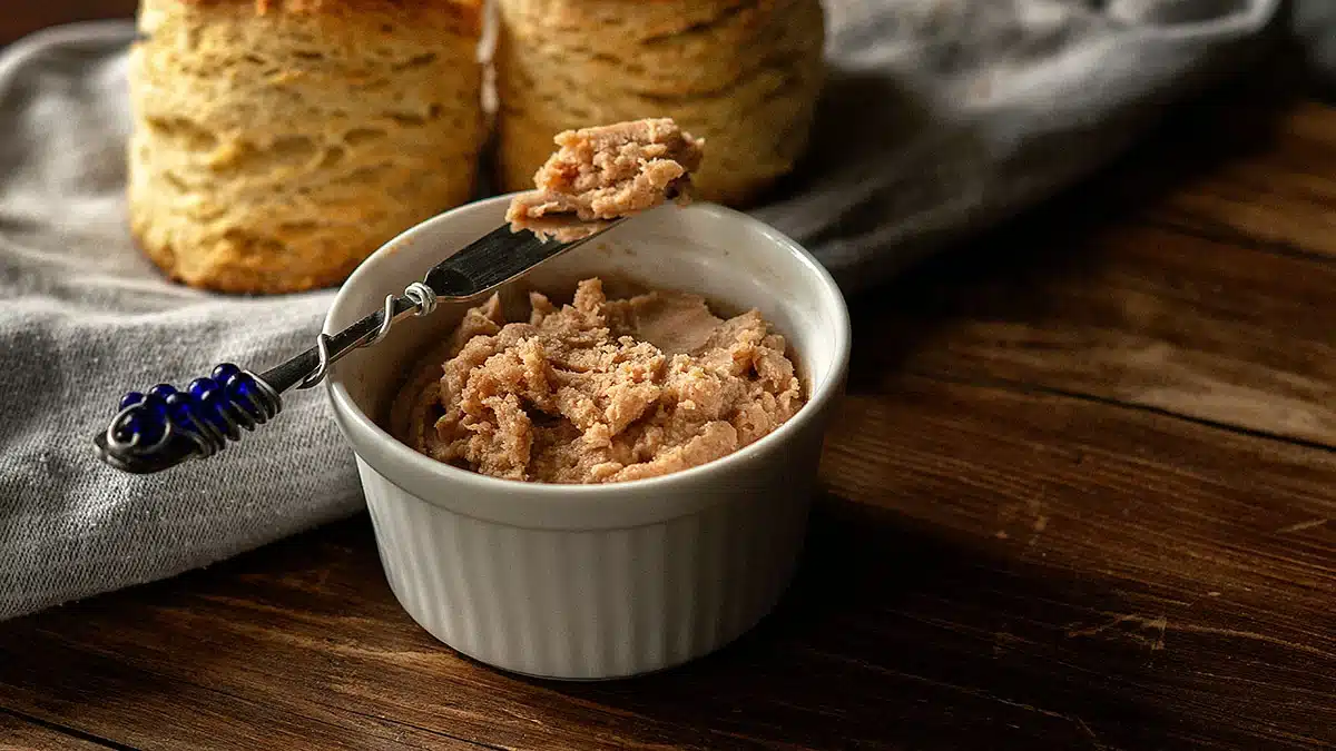 A ramekin of cinnamon butter with a knife, biscuits, and a cloth on a wooden table.
