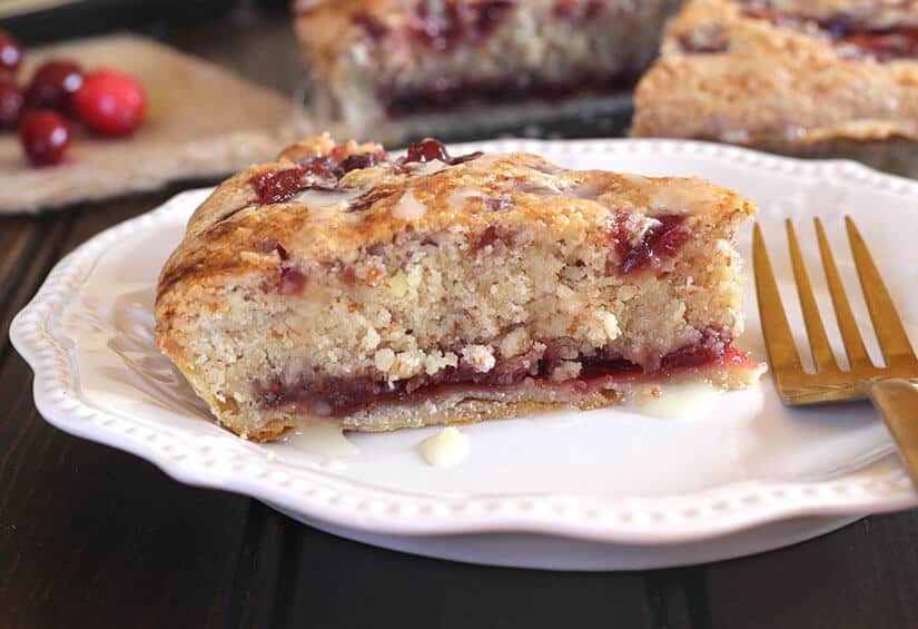 A slice of crumbly cake with berry filling on a white plate, next to a fork.