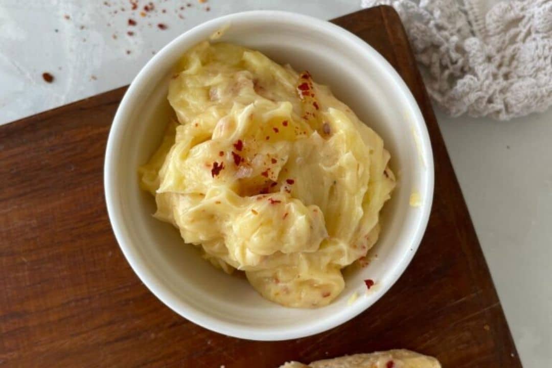 Creamy garlic aioli in a small white bowl, topped with red chili flakes, on a wooden board.