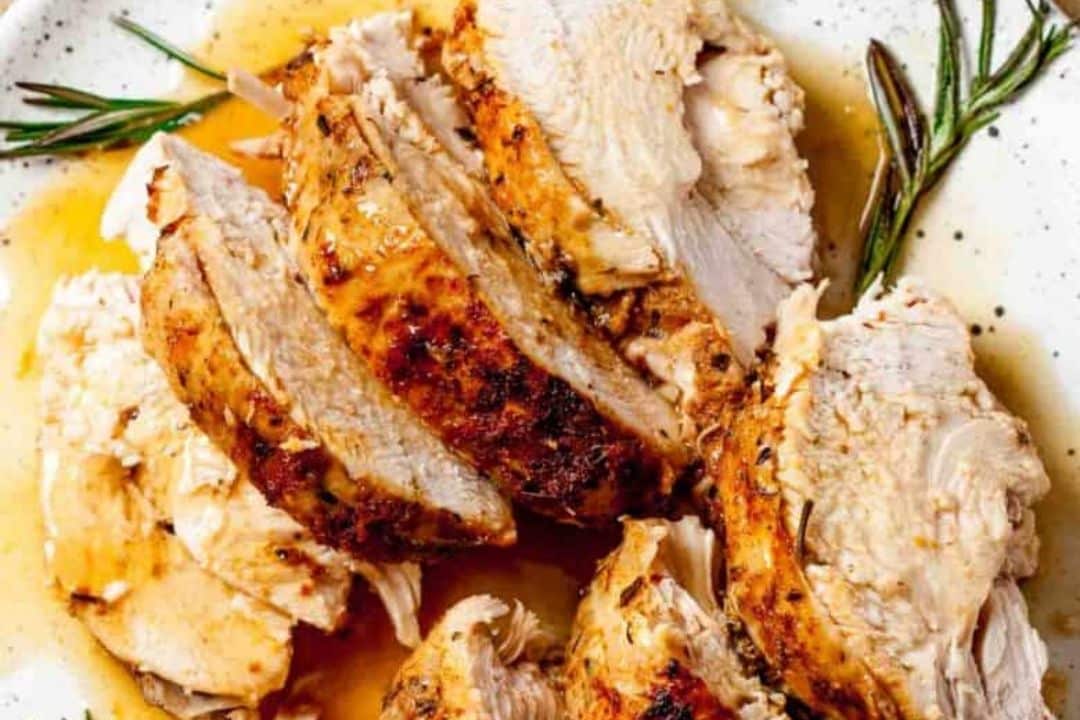 Sliced roasted turkey breast with herbs and gravy on a plate.