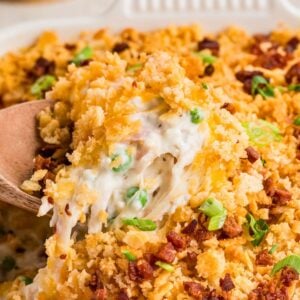 A wooden spoon lifts cheesy, creamy casserole with crispy topping, peas, and green onions.
