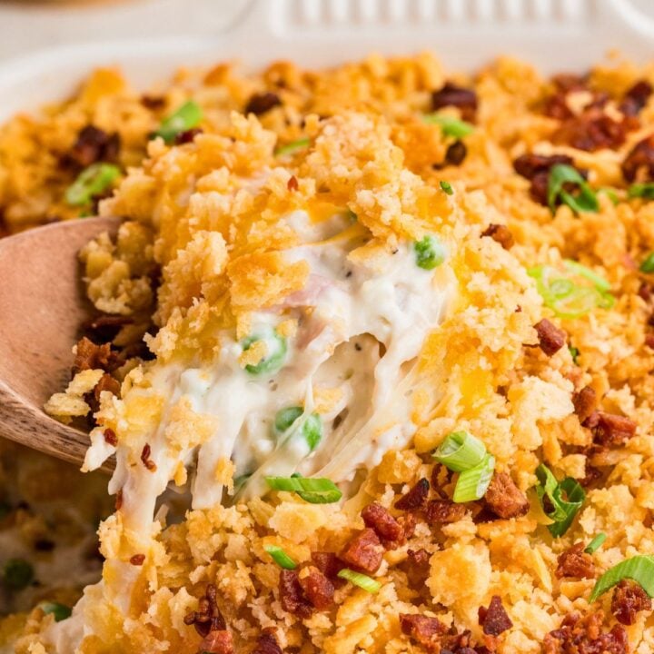 A wooden spoon lifts cheesy, creamy casserole with crispy topping, peas, and green onions.