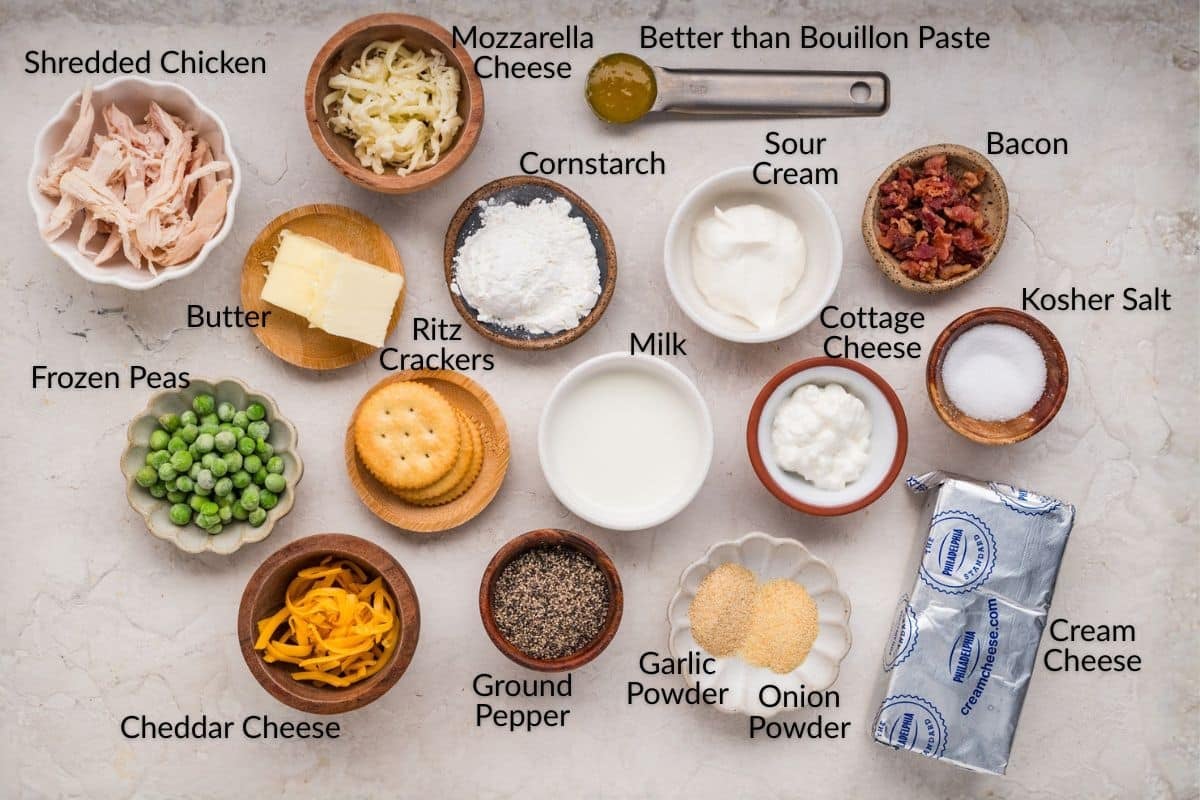 Ingredients for a casserole, including cheeses, peas, crackers, bacon, seasonings, milk, and butter on a counter.