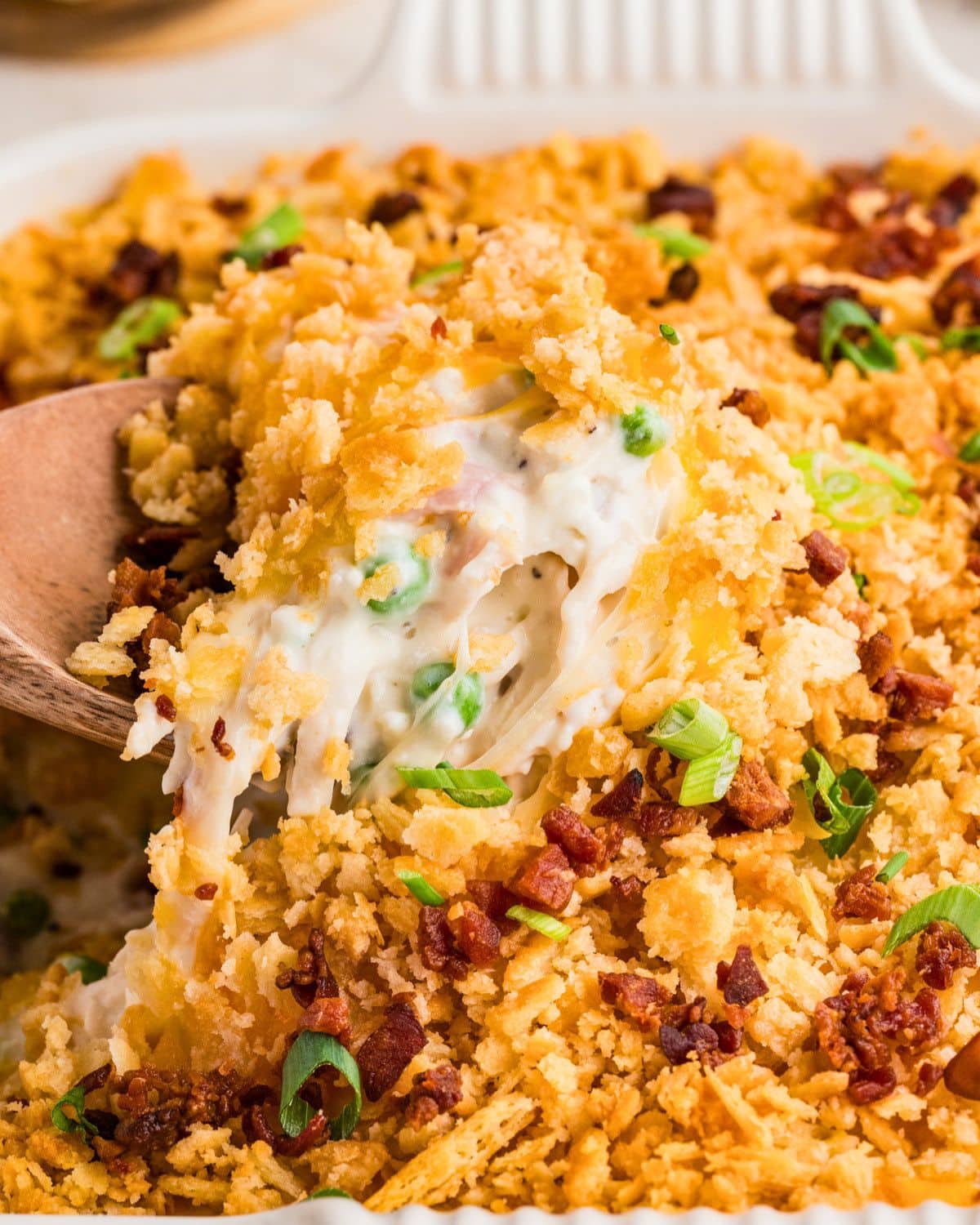 Spoonful of creamy casserole with peas, bacon bits, green onions, and a crispy golden topping.