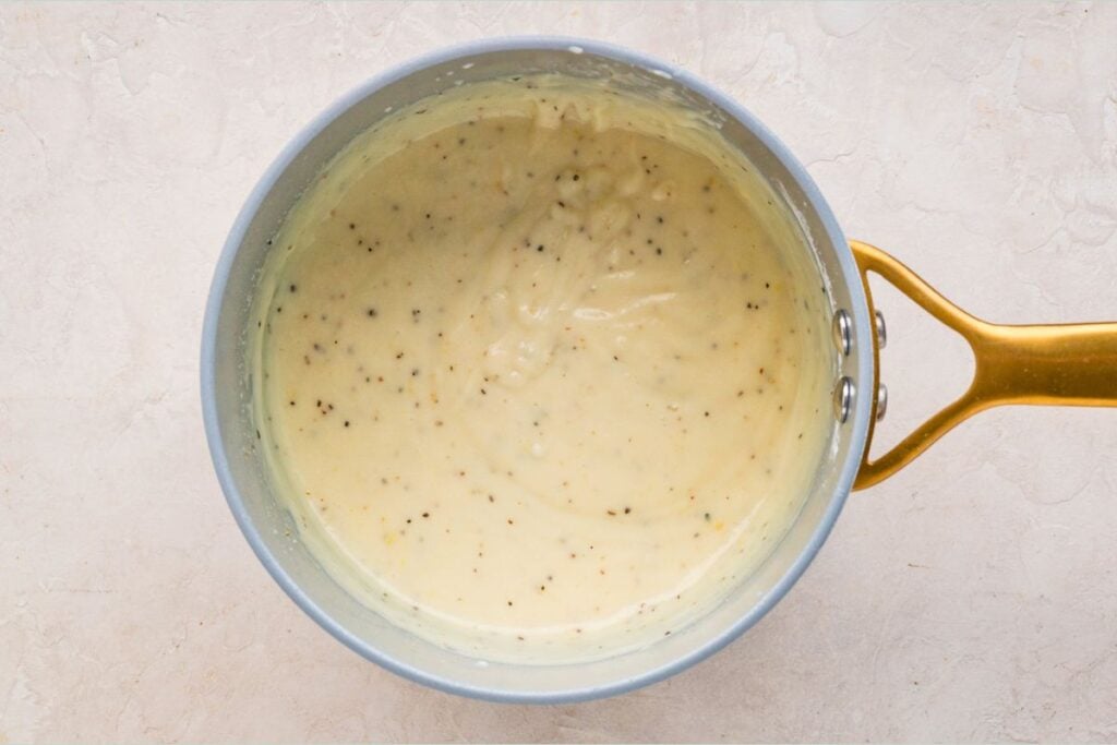 A saucepan filled with creamy white sauce with specks of pepper, shown from above on a light surface.