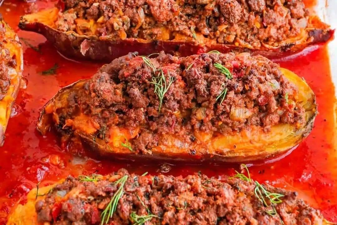 Baked eggplants stuffed with spiced ground meat and herbs, topped with tomato sauce.