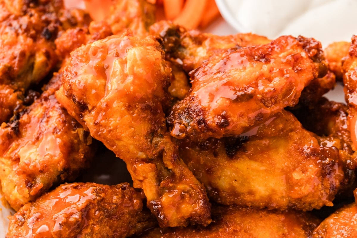 A pile of buffalo-style chicken wings with a side of dipping sauce and carrot sticks.