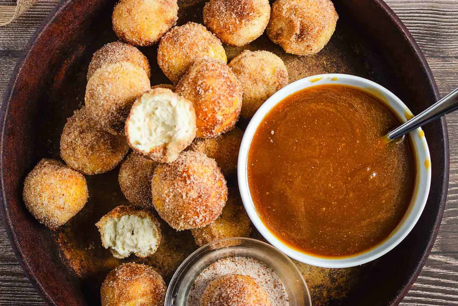 Cinnamon sugar donut holes in a pan with a side of dipping sauce.