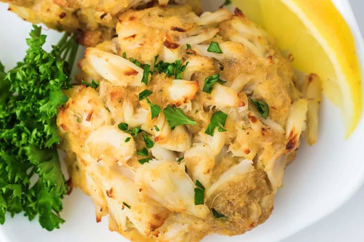 A crab cake garnished with parsley and served with a lemon wedge.