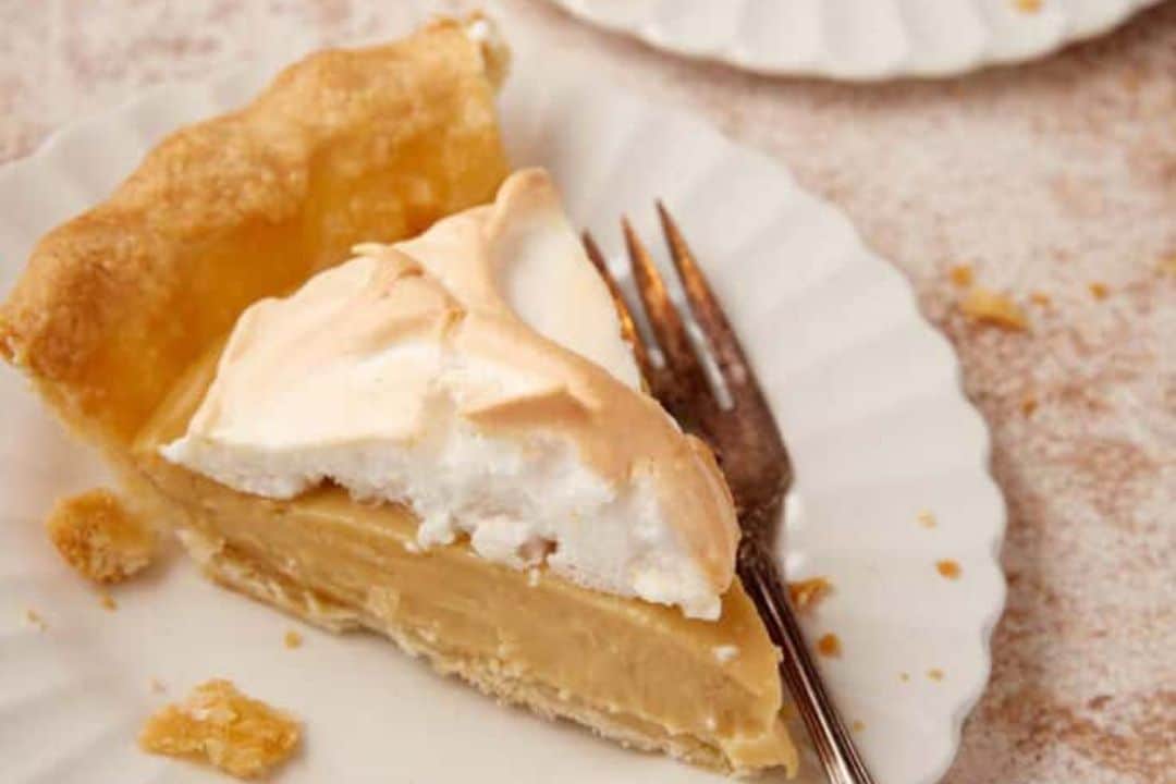 A slice of meringue pie on a white plate with a fork.