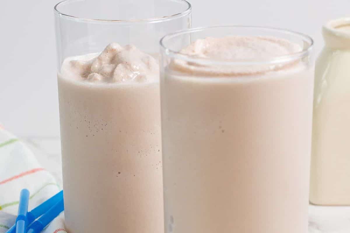 Two tall glasses filled with a light brown blended smoothie or milkshake.