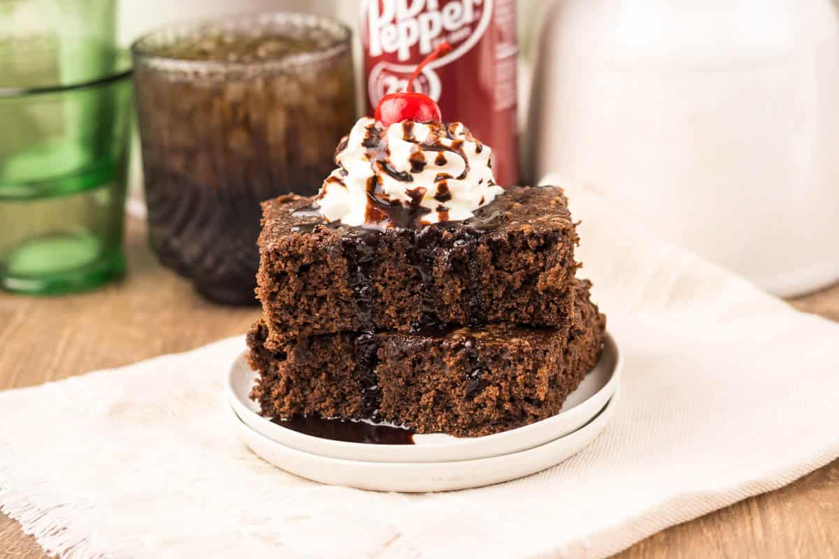 Two stacked chocolate brownies topped with whipped cream, chocolate syrup, and a cherry.