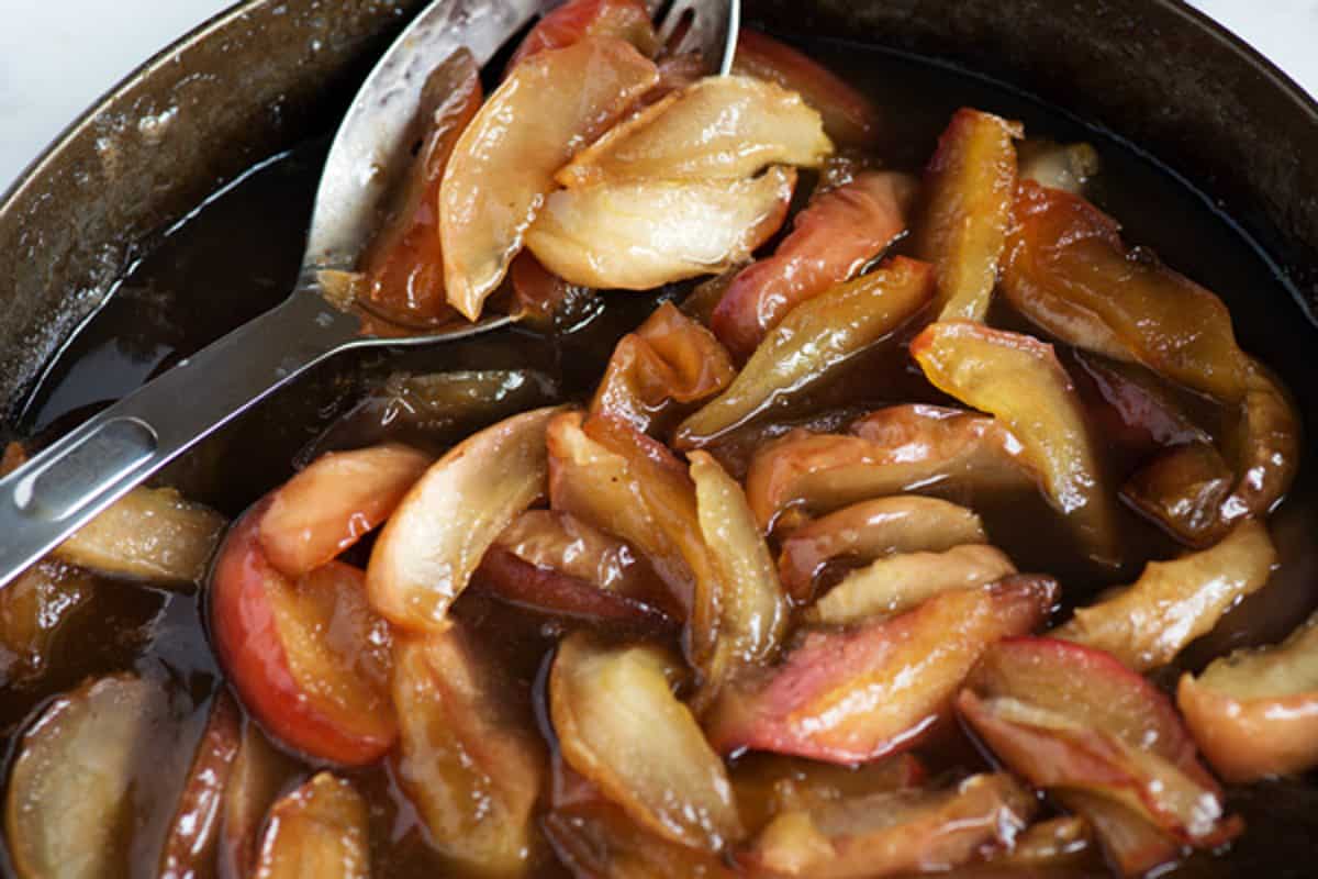Sautéed sliced apples in a pan with a metal serving spoon.