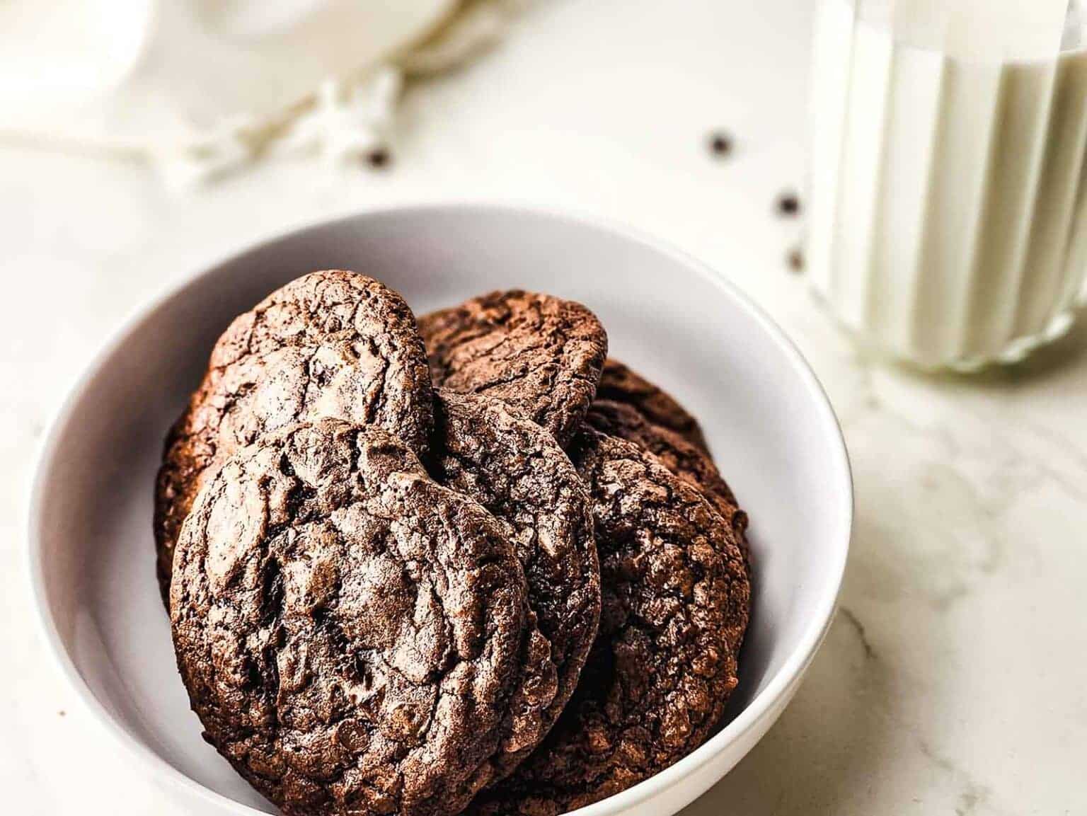 A bowl of chocolate cookies next to a glass of milk.