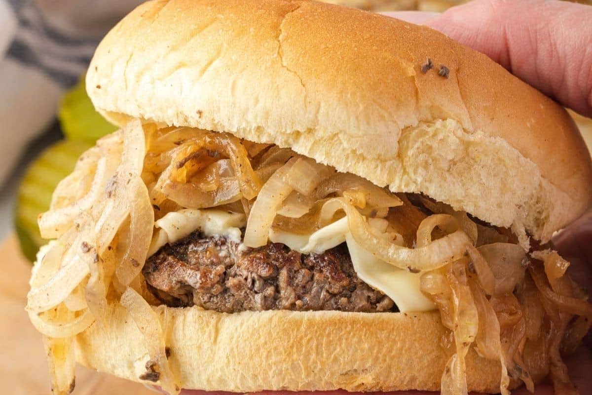 A cheeseburger topped with a generous portion of caramelized onions held in a hand.