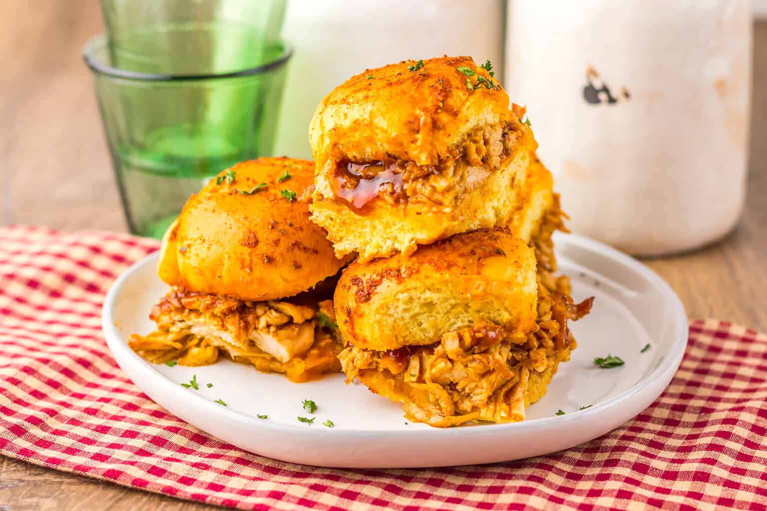 A stack of three pulled chicken sliders on a white plate.