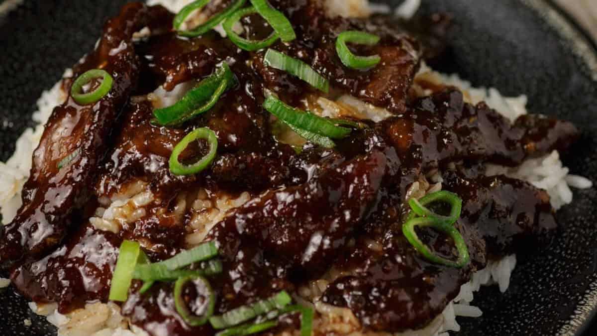 Beef in dark sauce served over white rice, garnished with sliced green onions.
