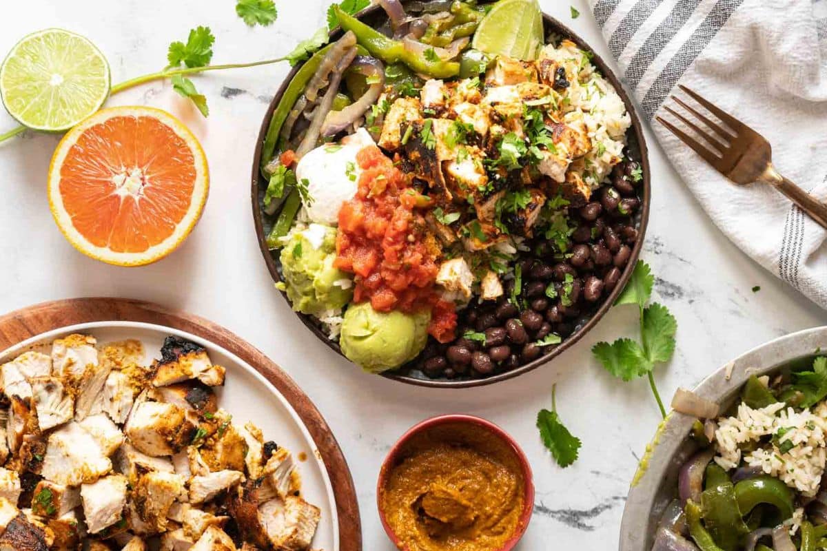 A chicken burrito bowl with black beans, guacamole, salsa, and lime, served with extra chicken and sauce.