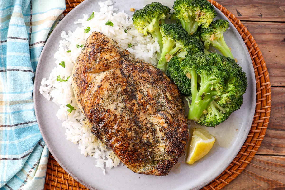 Seasoned chicken breast with white rice, broccoli, and a lemon wedge on a plate.