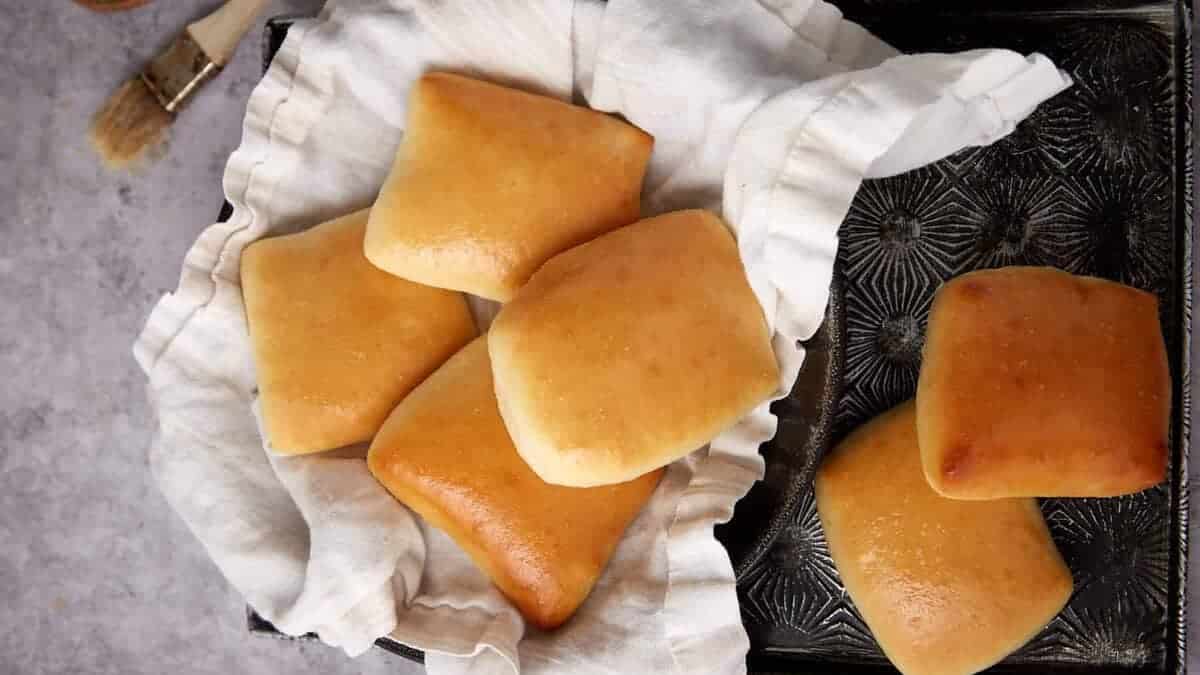 A tray of golden-brown square dinner rolls lined with a white cloth.