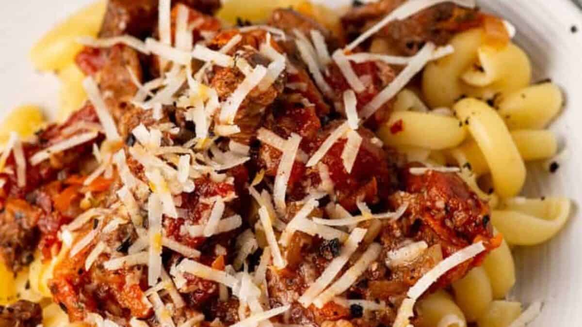 Pasta topped with a meat and tomato sauce, garnished with shredded cheese.