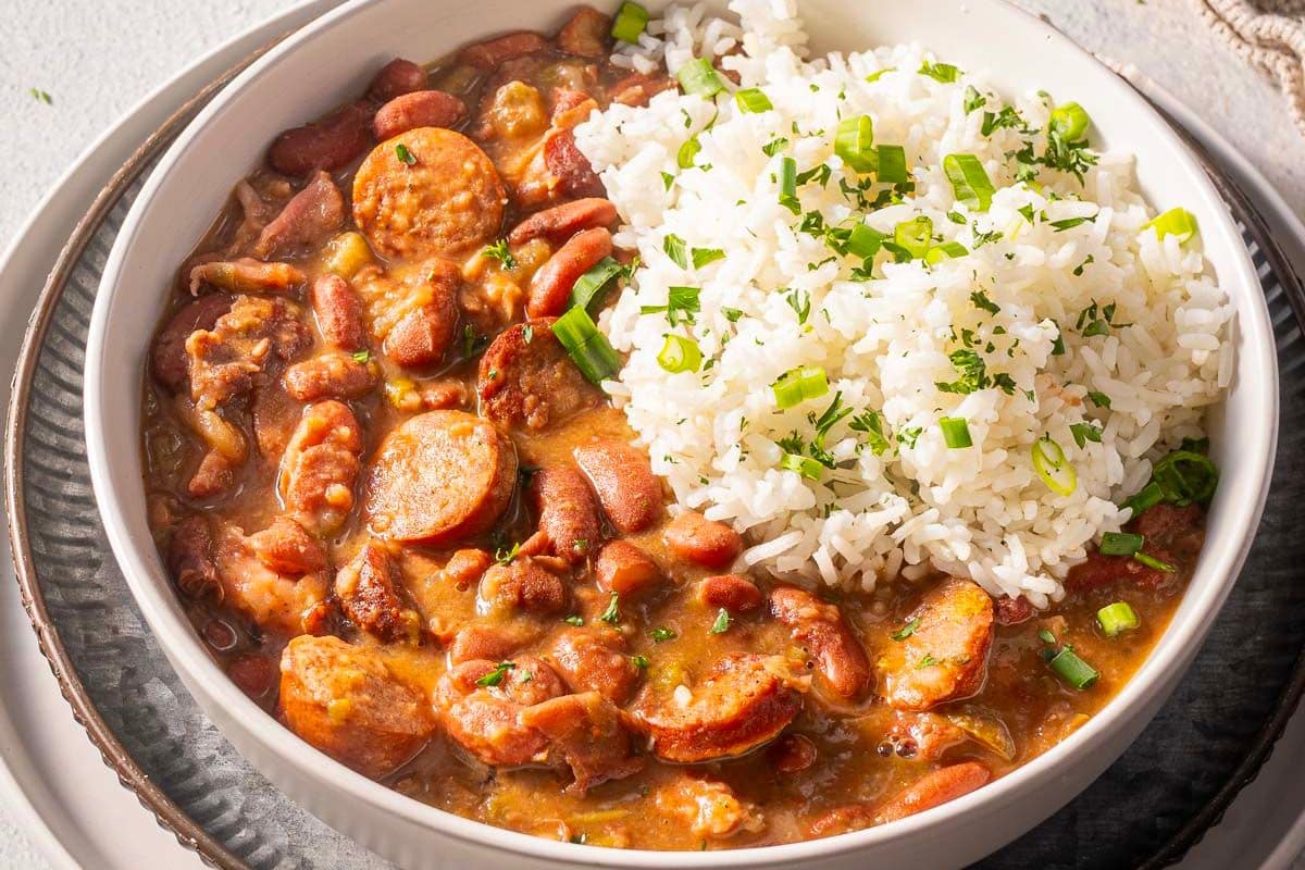 A bowl of red beans and rice with sliced sausage, topped with green onions.