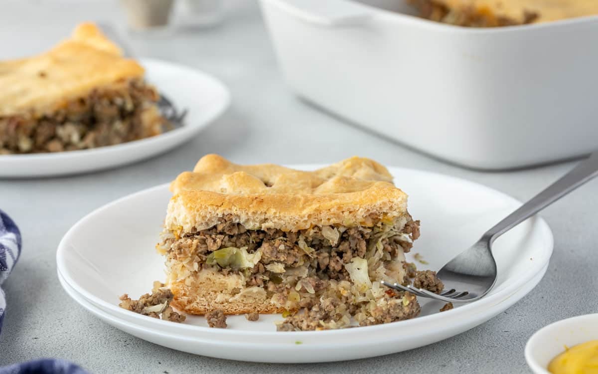 A slice of meat and cabbage pie on a white plate with a fork.