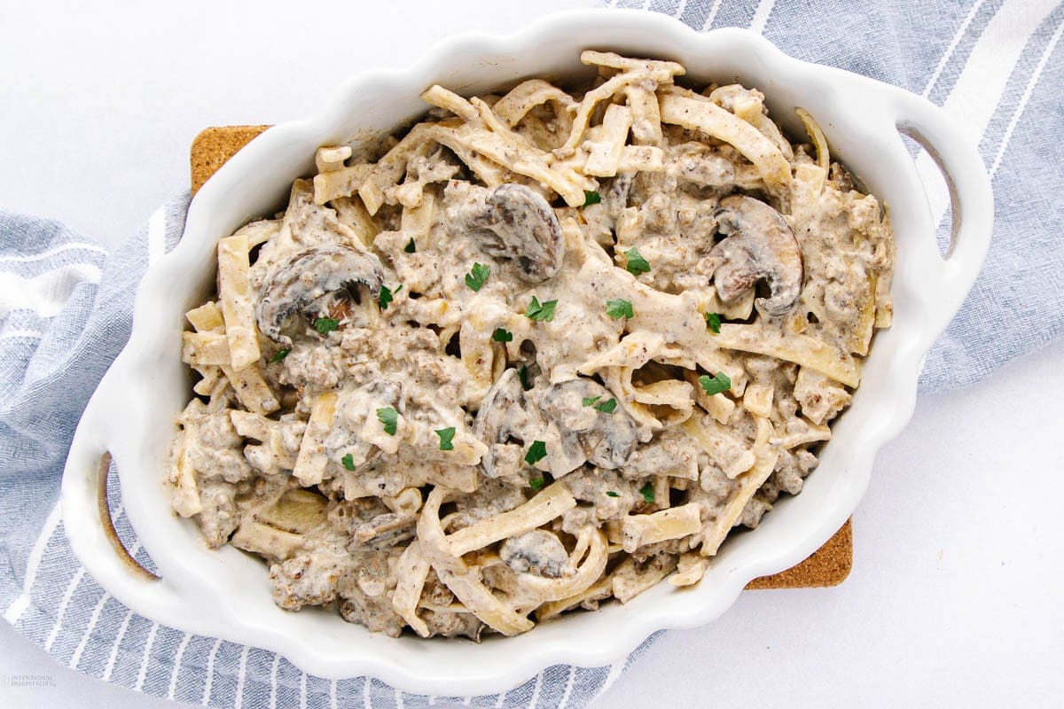 Baking dish filled with beef stroganoff pasta topped with mushrooms and herbs.