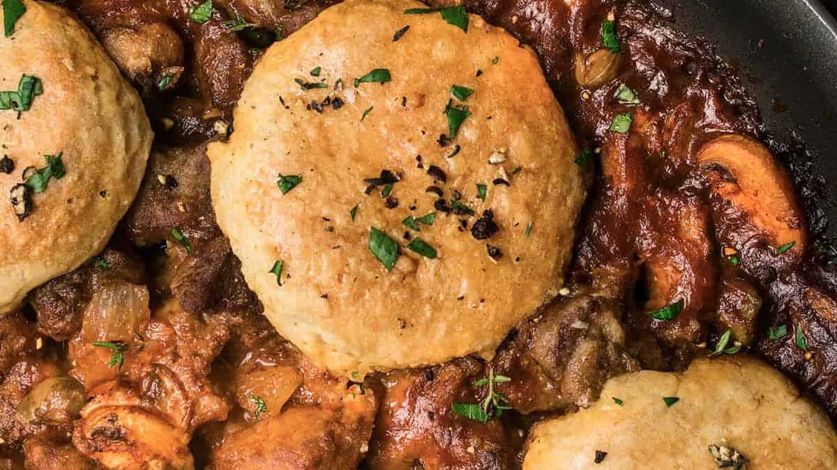Beef stew in a skillet topped with biscuits and herbs.