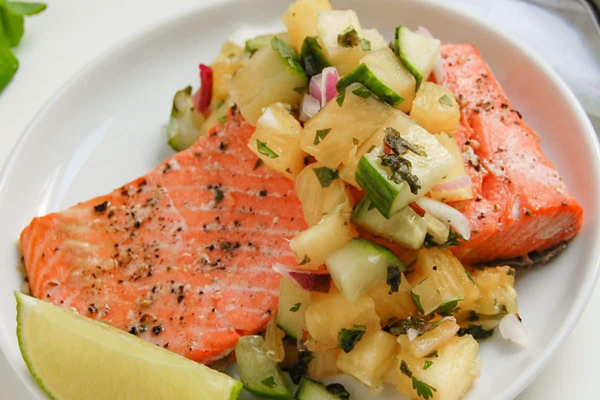 Cooked salmon fillet topped with pineapple and cucumber salsa, served with a lime wedge.
