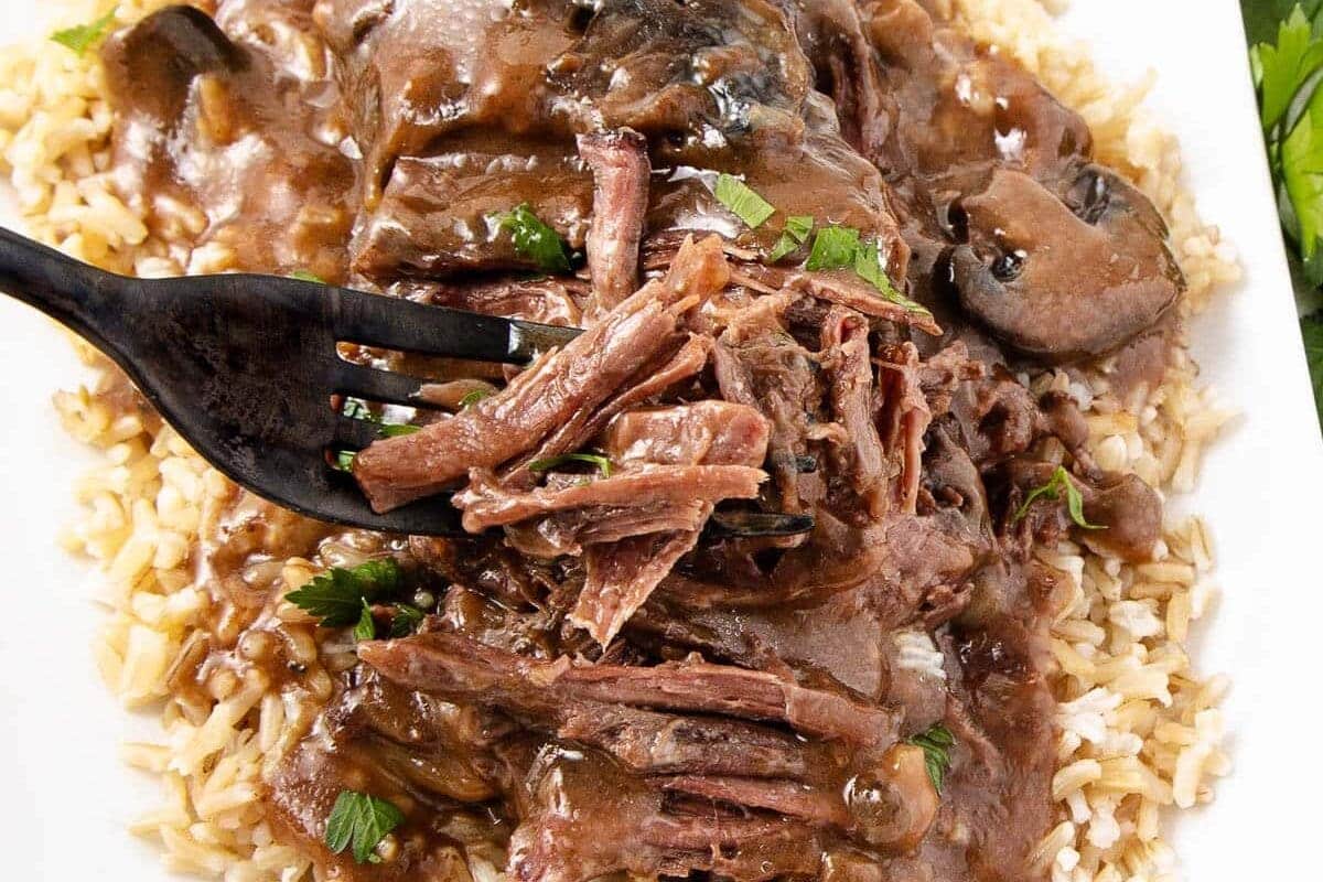 A fork lifting shredded beef with mushroom gravy over a bed of brown rice.