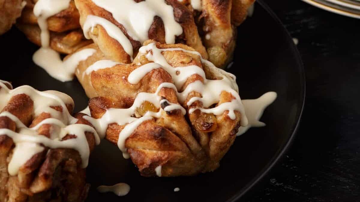 Cinnamon rolls with raisins drizzled with white icing on a black plate.