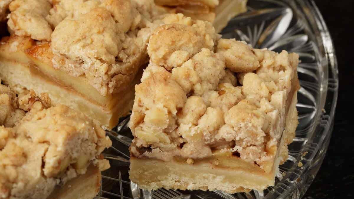 Squares of apple crumble bars on a glass serving platter.