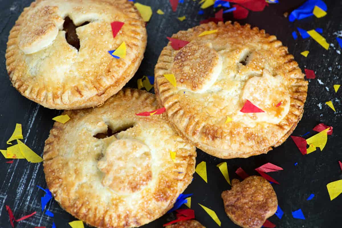 Three golden-brown hand pies surrounded by colorful confetti on a dark surface.