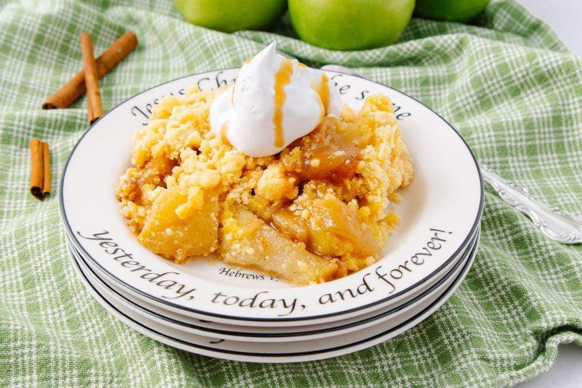 A serving of apple crisp topped with whipped cream and caramel sauce on a plate.