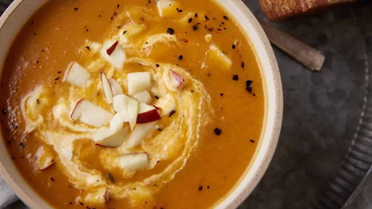 A bowl of pureed soup topped with cream and chopped apples.