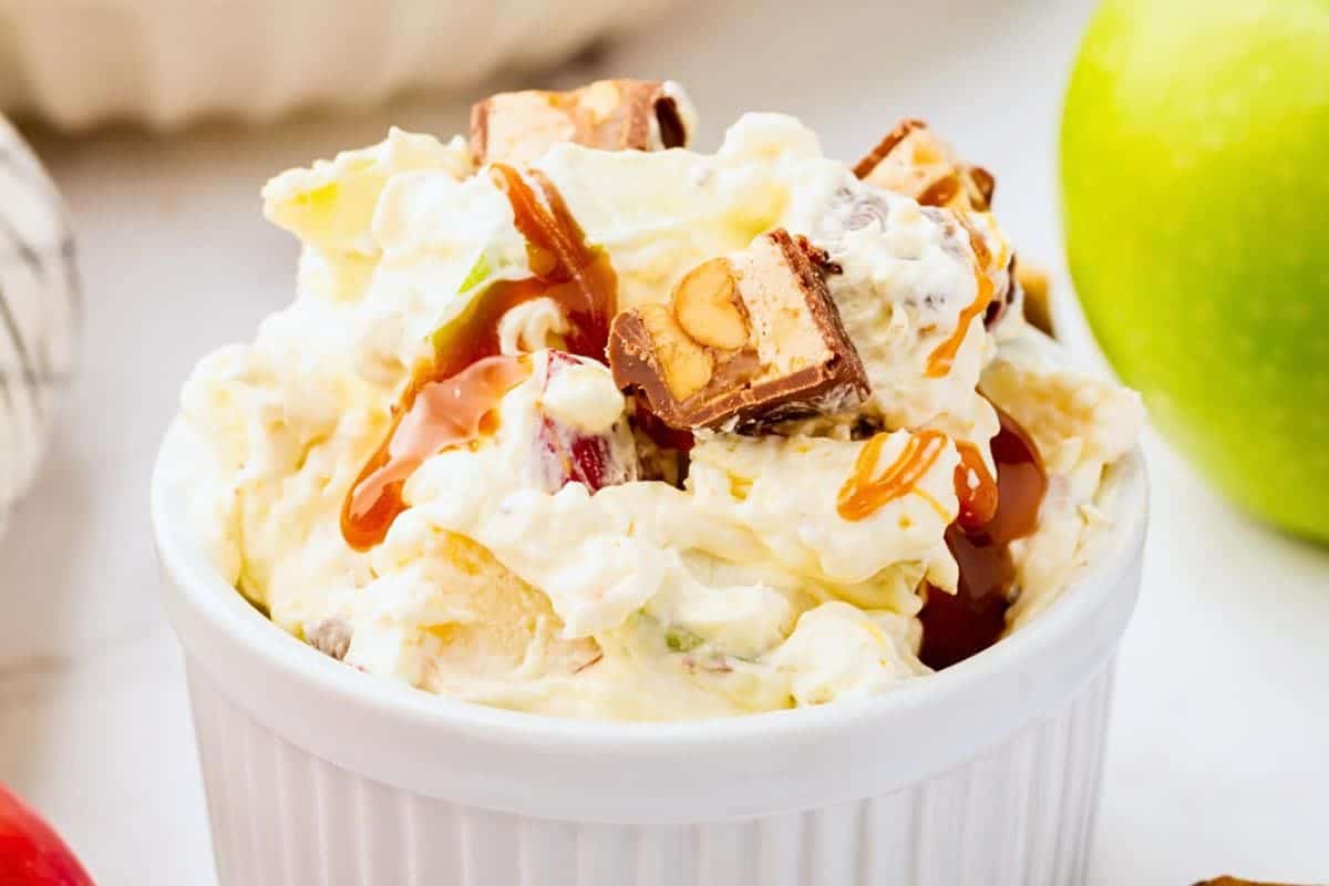 Apple snickers salad in a white bowl, drizzled with caramel sauce.