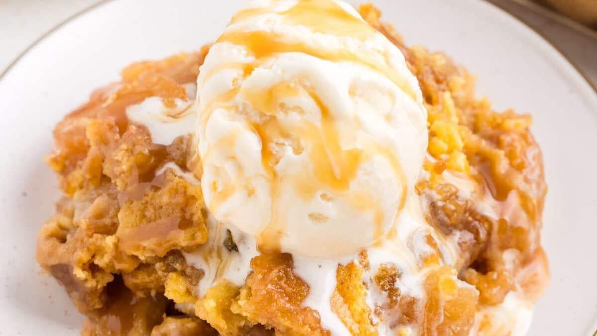 A scoop of vanilla ice cream topped with caramel sauce on a serving of warm cobbler.